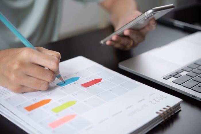 Une personne prend des notes sur un calendrier en consultant son portable